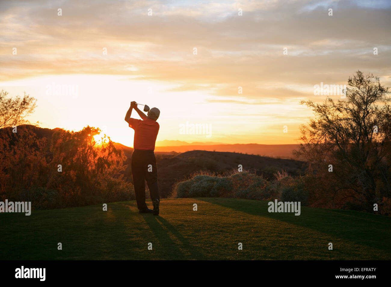 Prendre un golfeur swing sur le raccord en t avec vue sur le paysage d'un terrain de golf au crépuscule dans l'Arizona. Banque D'Images