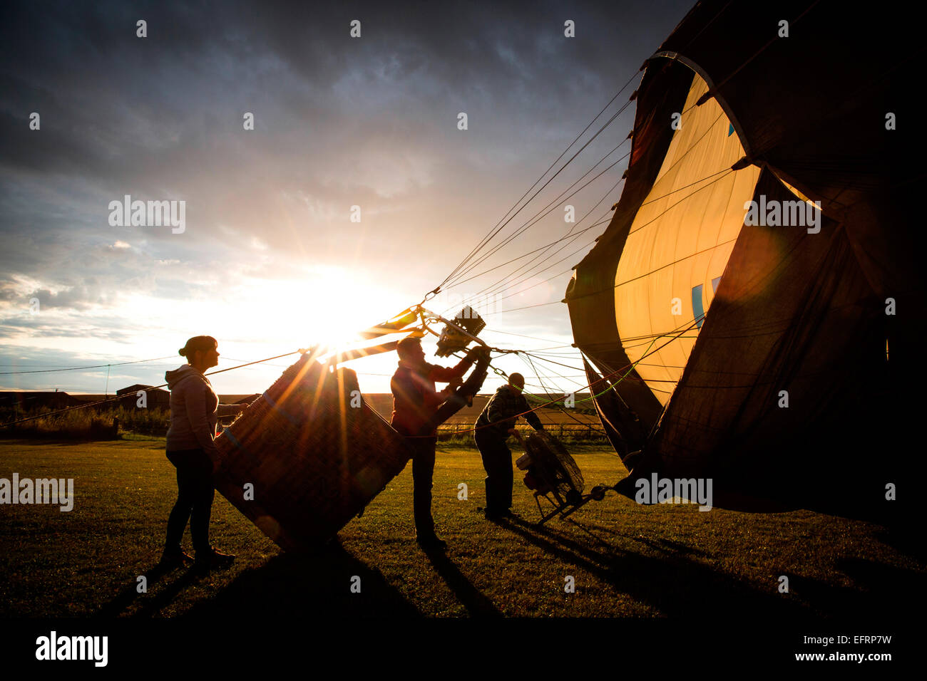 Le gonflage de l'équipage d'accueil hot air balloon at sunset, south Oxfordshire, Angleterre Banque D'Images