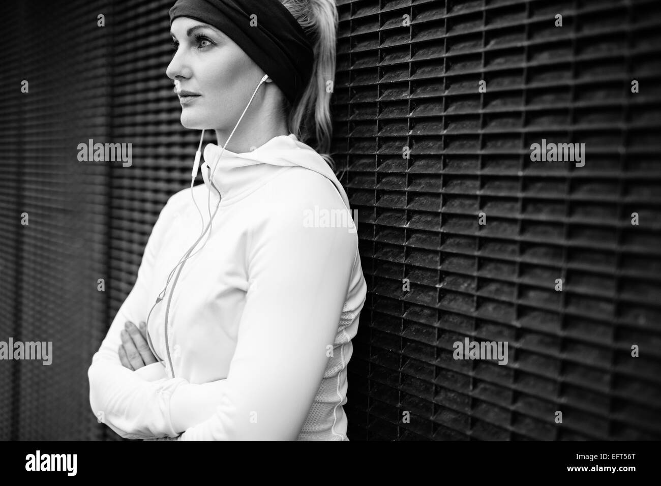 Image en noir et blanc de jeune femme portant un mur permanent écouteurs se penchant à la route en toute confiance. Femme de remise en forme au repos. Banque D'Images