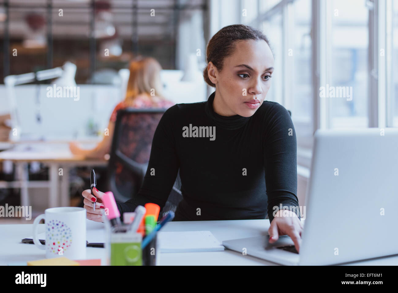 Image de jeune femme travaillant sur un ordinateur portable tout en étant assis à son bureau dans un bureau moderne. La direction de l'Afrique au travail. Banque D'Images