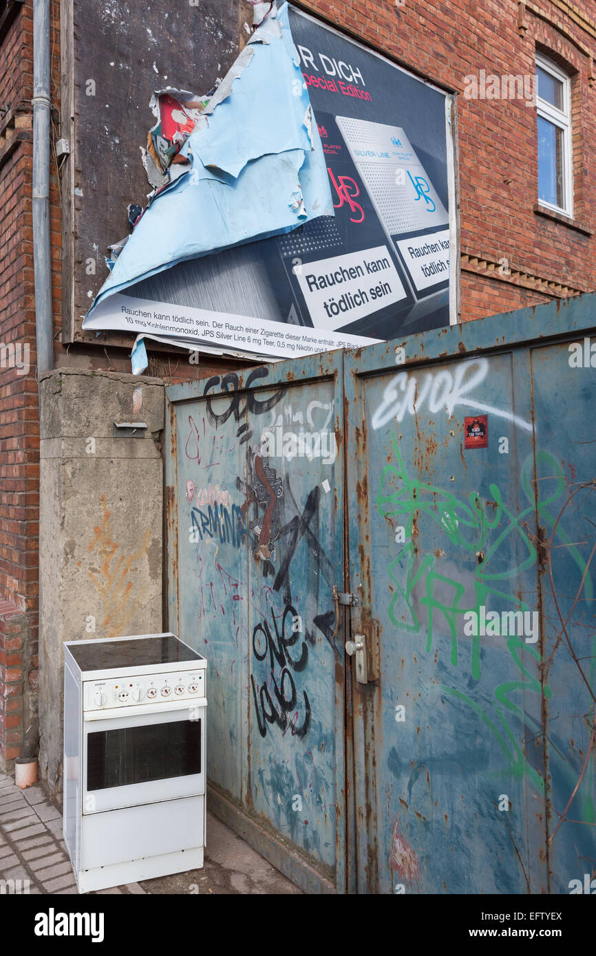 Une vieille cuisinière électrique se trouve dans la rue, à côté d'une barrière métallique recouvert de graffitis et au-dessous d'un panneau publicitaire de déroulage Banque D'Images