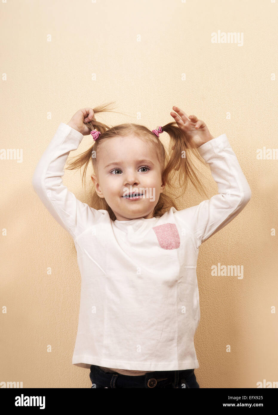 Peu playful girl holding her queues, vertical studio portrait Banque D'Images