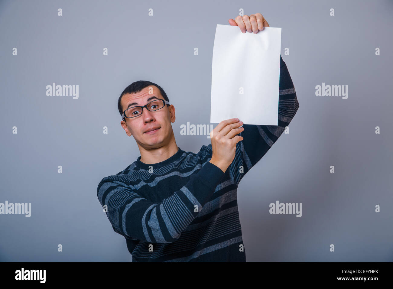 Homme européen tenant une feuille de papier blanc sur un fond gris b Banque D'Images