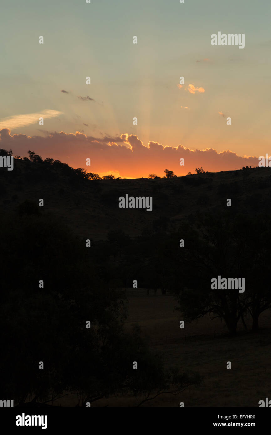 Une version non révisée (RAW) Photographie de la soleil derrière quelques collines. Le soleil est obscurci par des nuages bas. Banque D'Images