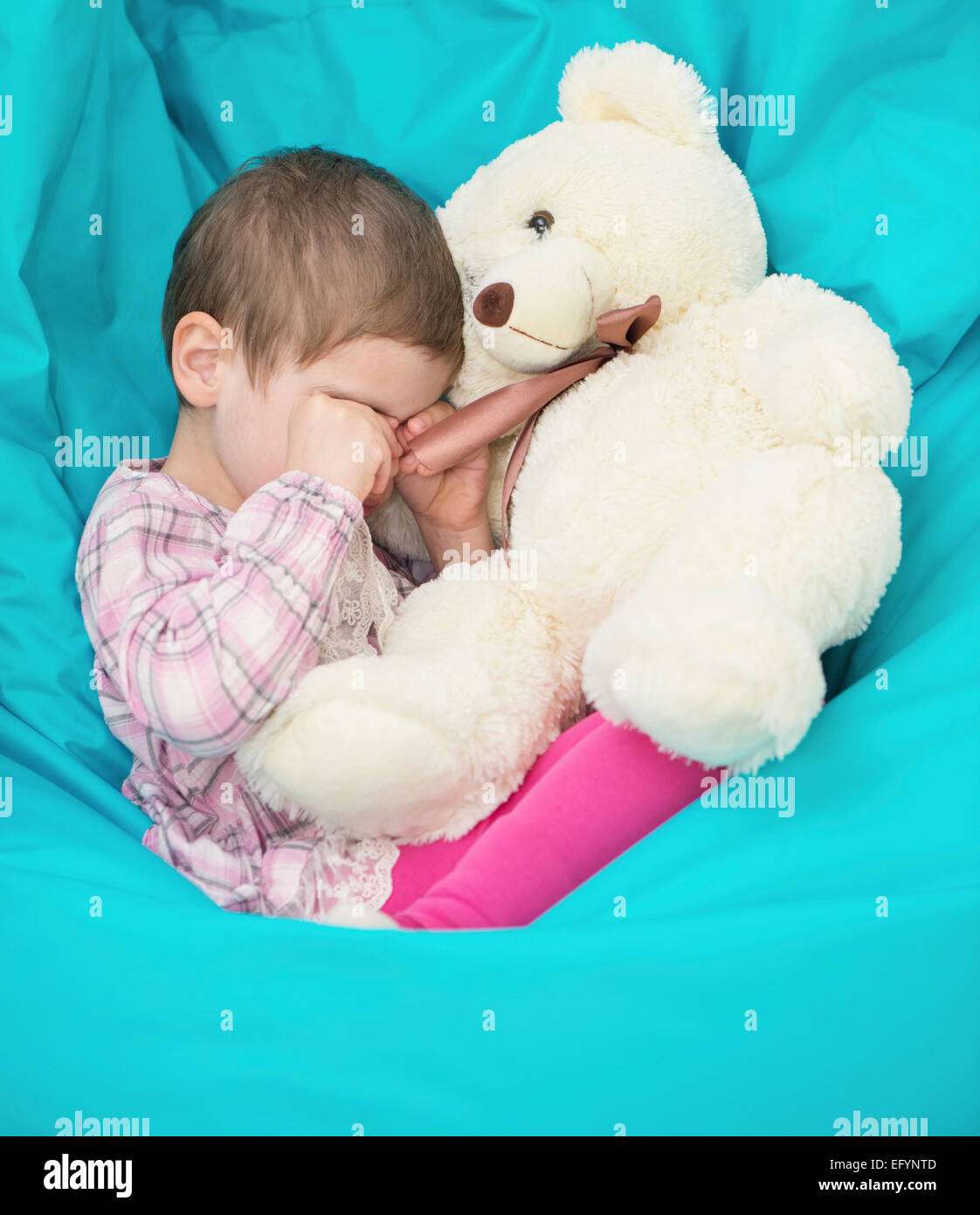 Petite fille assise en pleurs avec pouf ours blanc Banque D'Images