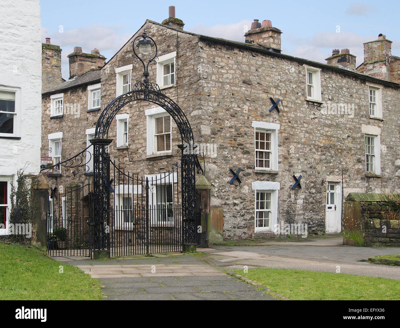 Portes en fer forgé de l'église Sainte Marie de Kirkby Lonsdale, une ville dans la région de Cumbria, montrant les cottages traditionnels en pierre. Banque D'Images