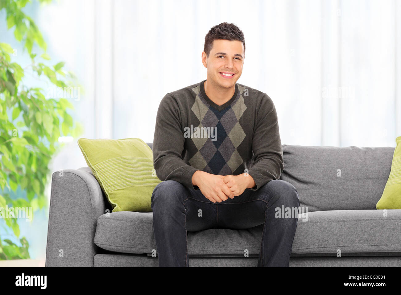 Jeune homme posant assis sur un canapé à la maison Banque D'Images