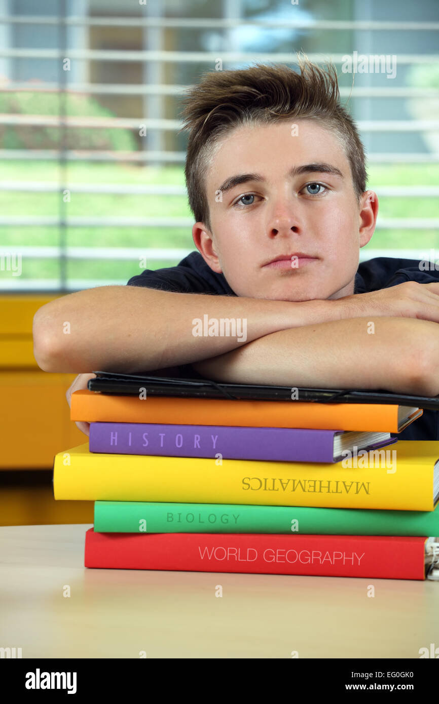 Photo d'un jeune adolescent s'appuyant sur ses livres, s'ennuie dans sa classe. Banque D'Images