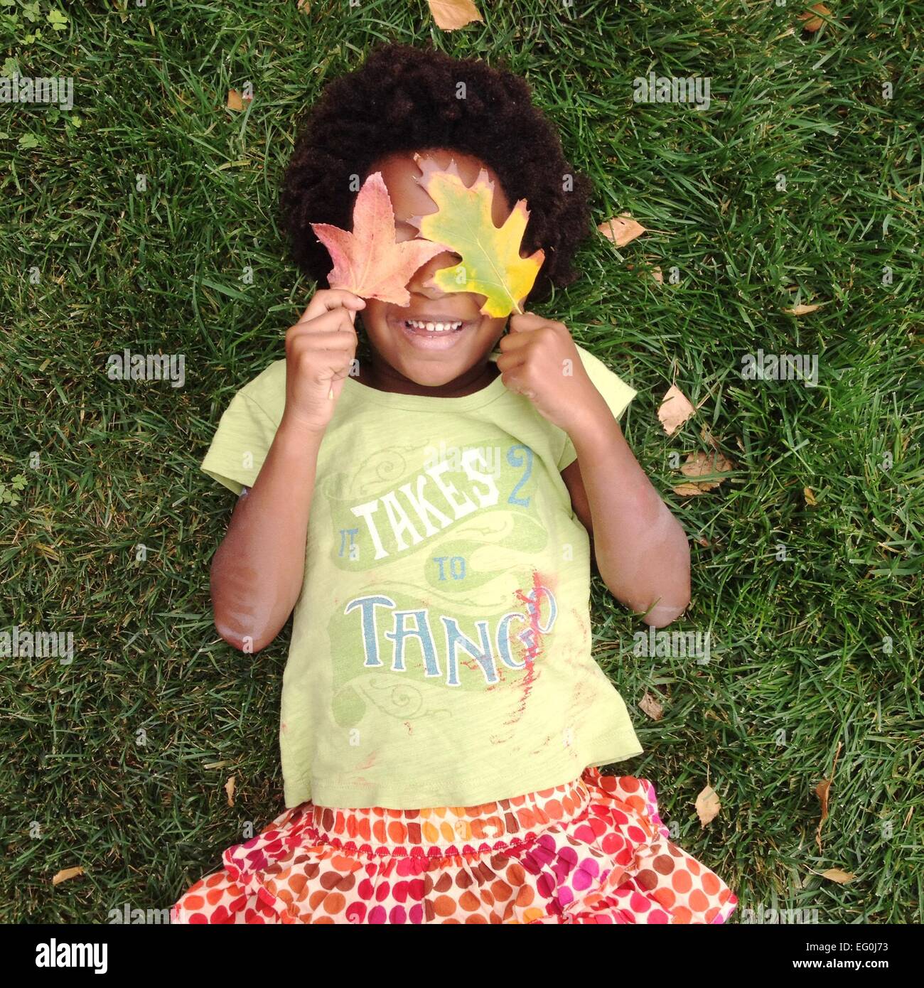 Girl lying on grass holding feuilles sur ses yeux Banque D'Images
