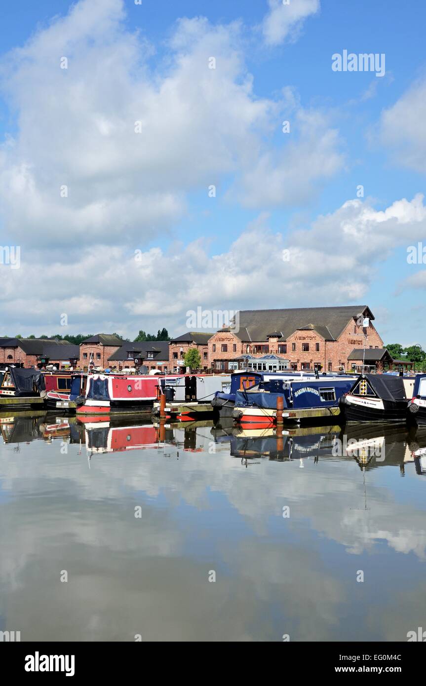 Narrowboats sur leurs amarres dans le bassin du canal, avec des magasins, bars et restaurants à l'arrière, Barton-under-Needwood, UK. Banque D'Images