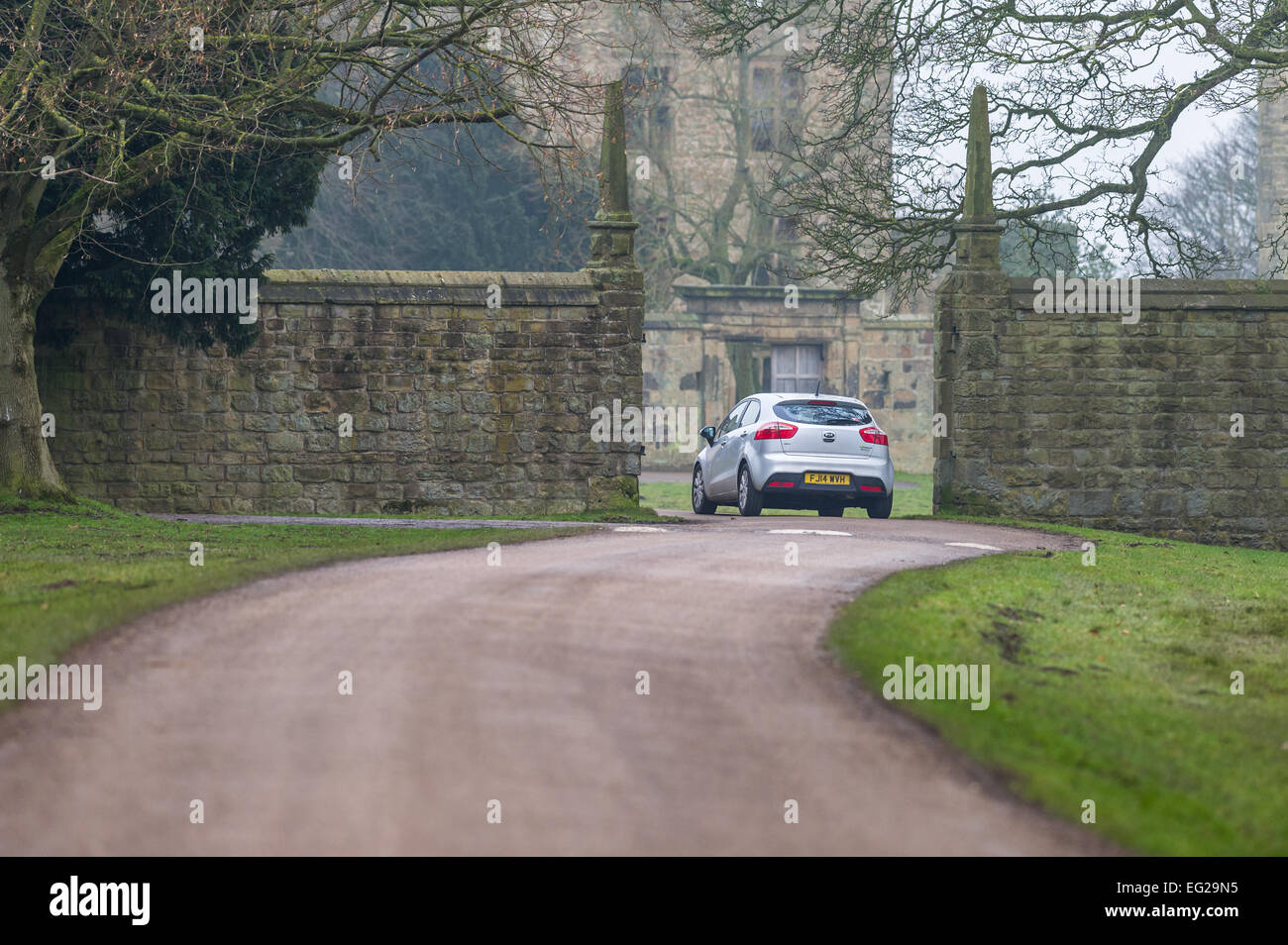 Voiture Kia blanc en passant par une vieille pierre élisabéthain gateway dans un parc de pays. Banque D'Images