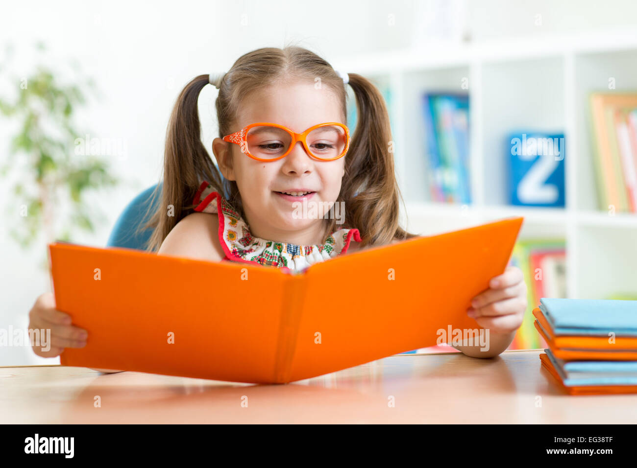 Happy funny girl enfant dans les verres de la lecture d'un livre à l'école primaire Banque D'Images