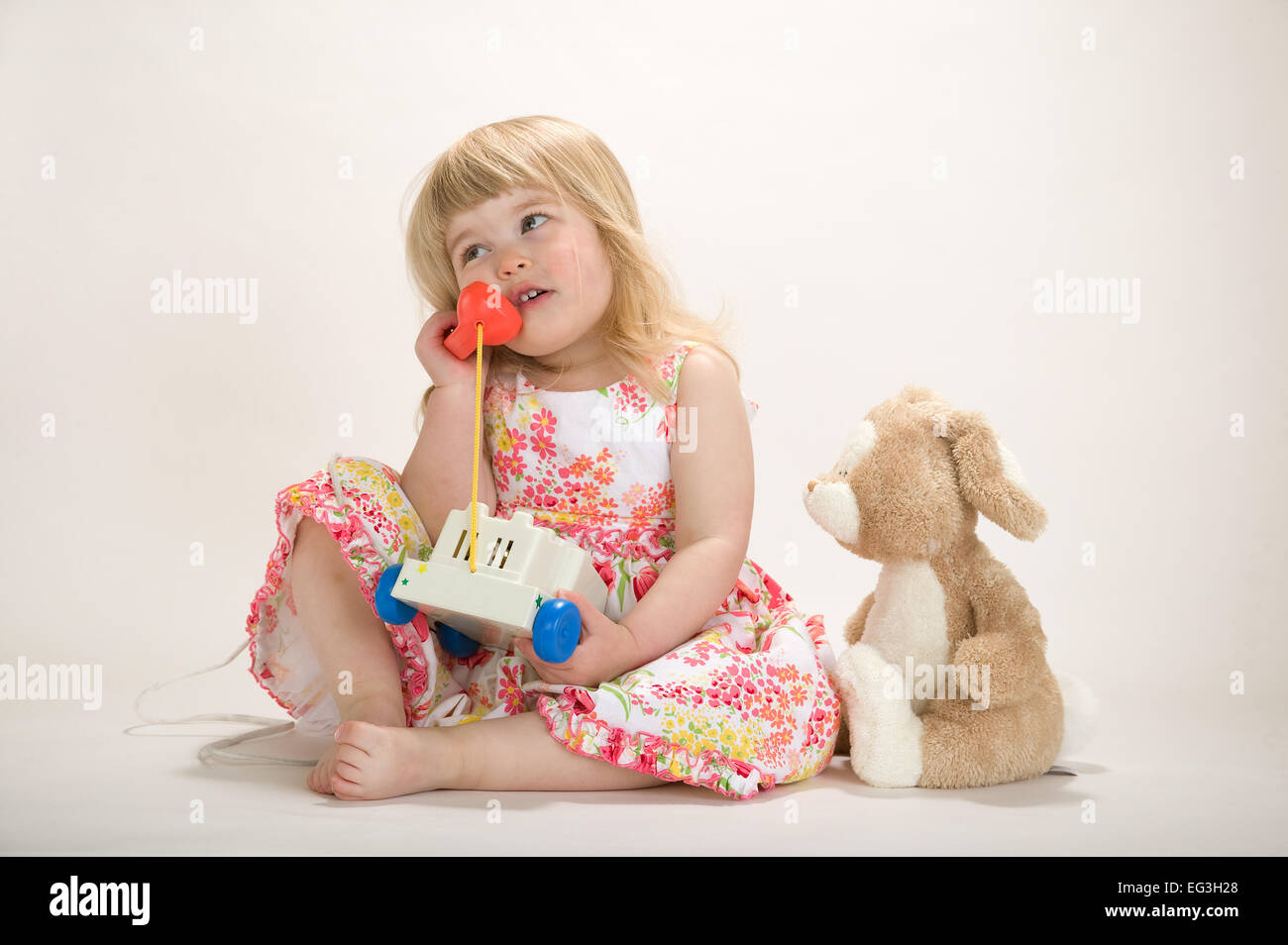 Bébé fille (2,5 ans) jouer, parler sur un jouet téléphone. Concepts : l'ennui, la lassitude, l'imagination, faire-croire Banque D'Images