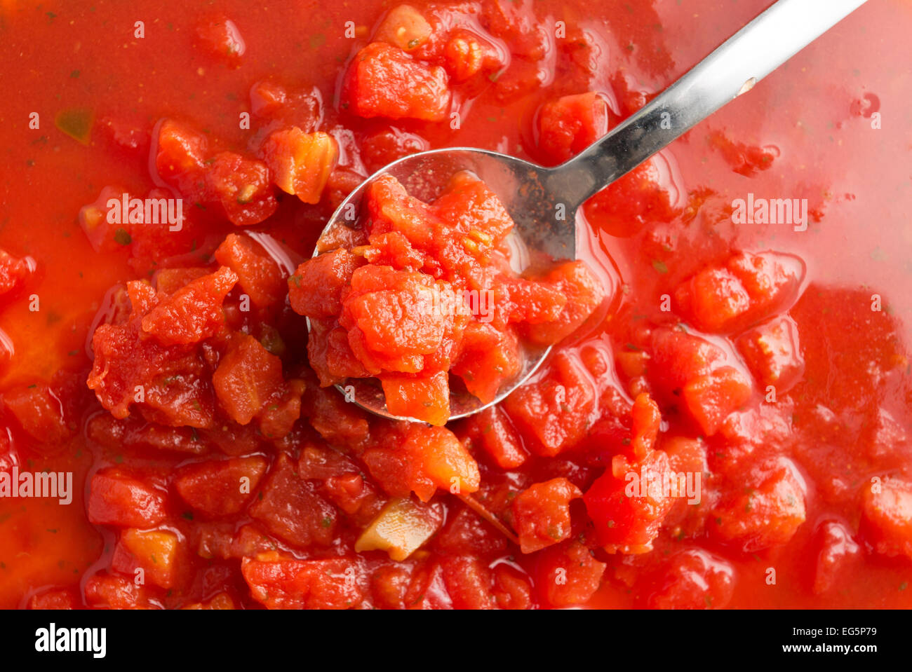 Fermer la vue de dés de tomates au jus de tomates avec piment jalapeño ajouté plus d'une cuillère en métal fenêtre illuminée par la lumière naturelle. Banque D'Images