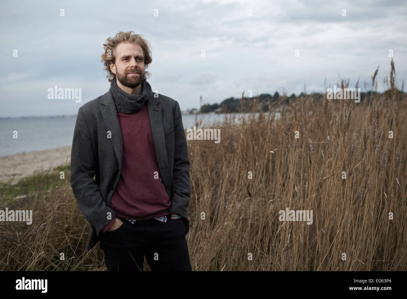 Un portrait d'un homme dans la trentaine debout entouré d'herbes et de roseaux au bord de la mer Banque D'Images