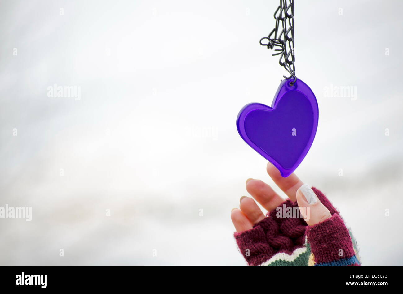 Femme dans les mains des mitaines pour atteindre le purple heart against a white background bokeh Banque D'Images