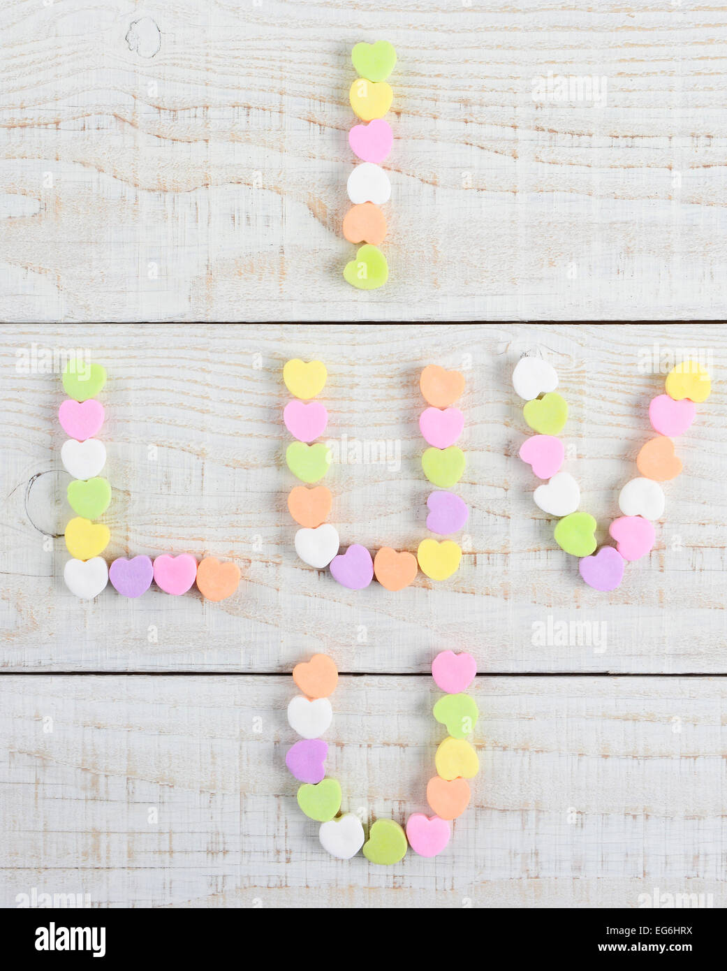 High angle shot d'un groupe de bonbons coeurs pastel Saint Valentin formant I Luv U sur une table en bois blanc rustique. Banque D'Images