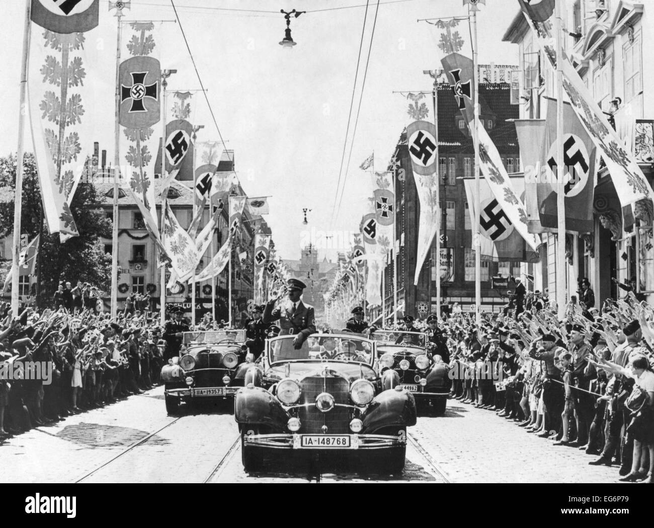 Adolf Hitler en agitant à la foule de sa voiture à la tête d'une parade. Les rues sont décorées de différentes bannières à croix gammée. Banque D'Images