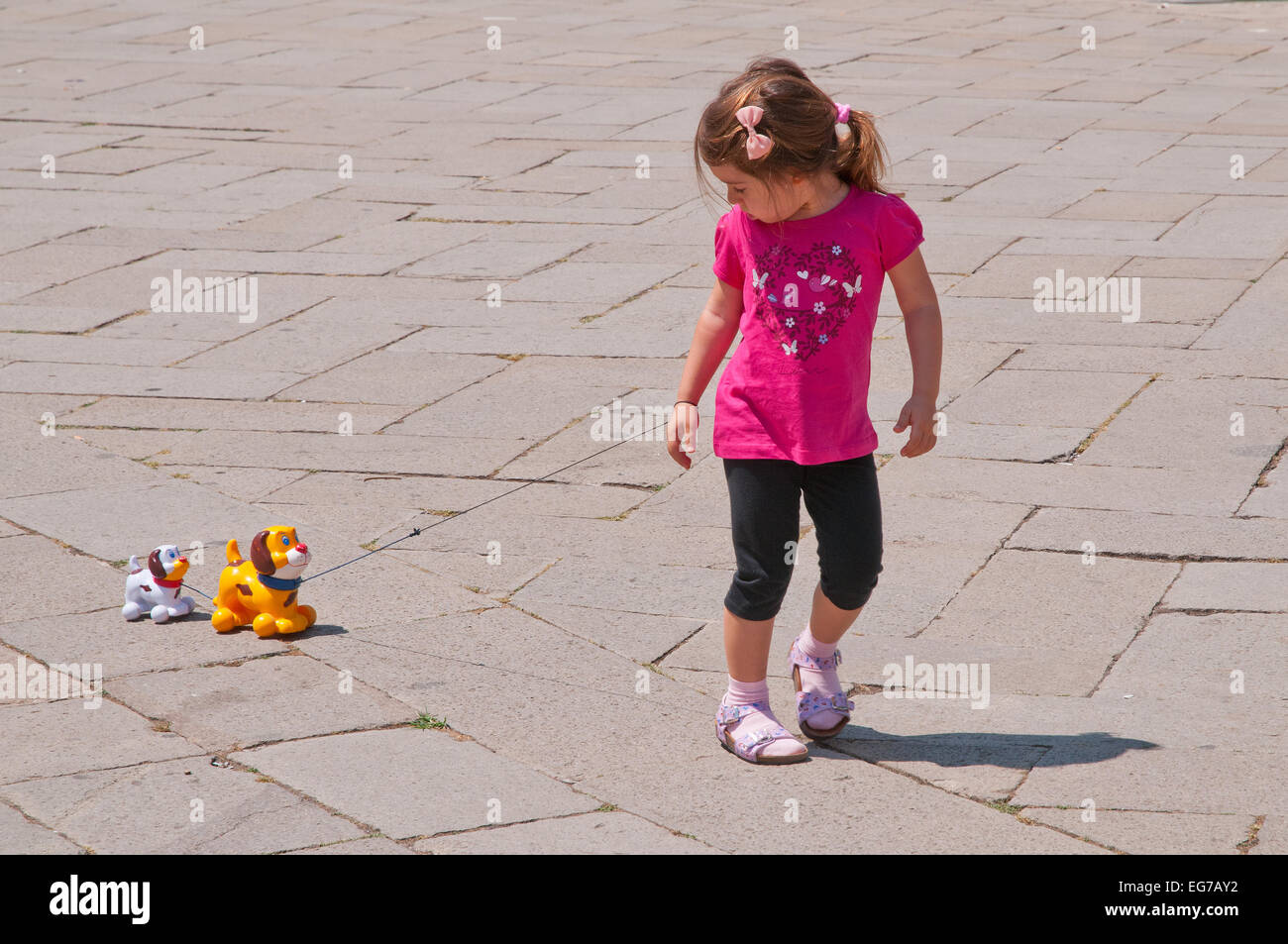 Jeune fille avec tee shirt rose décorée de fleurs et coeur tire deux chiens jouets sur chaîne dans Campo San Stefano Venise Italie Banque D'Images