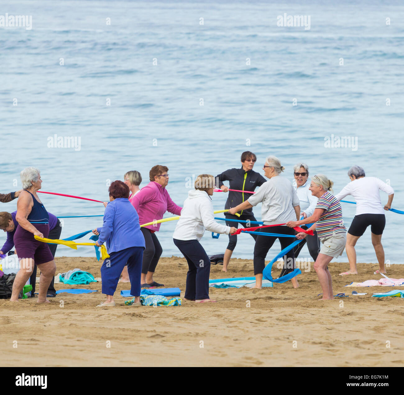Les femmes âgées à l'aide de bandes de résistance élastique au cours de l'exercice quotidien class sur la plage en Espagne Banque D'Images