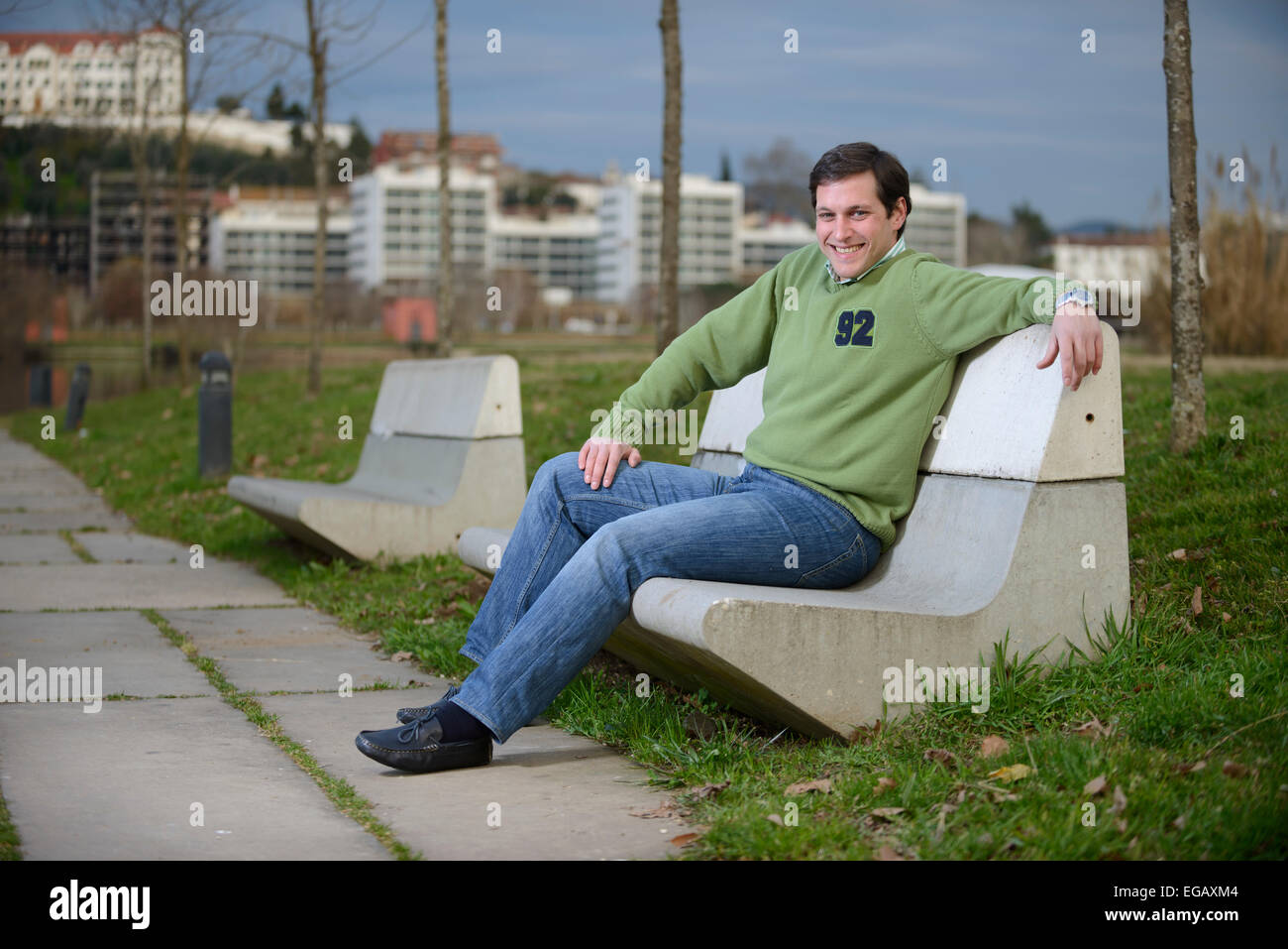 Jeune homme assis sur un banc en ciment dans un parc Banque D'Images