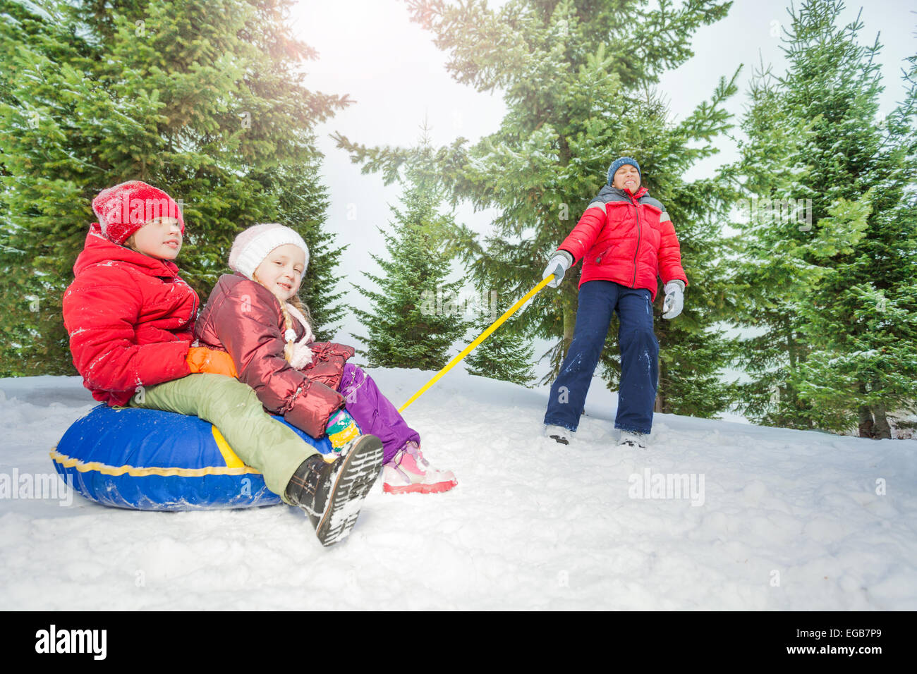 Enfants heureux assis sur snow tube et d'autres les tirant Banque D'Images
