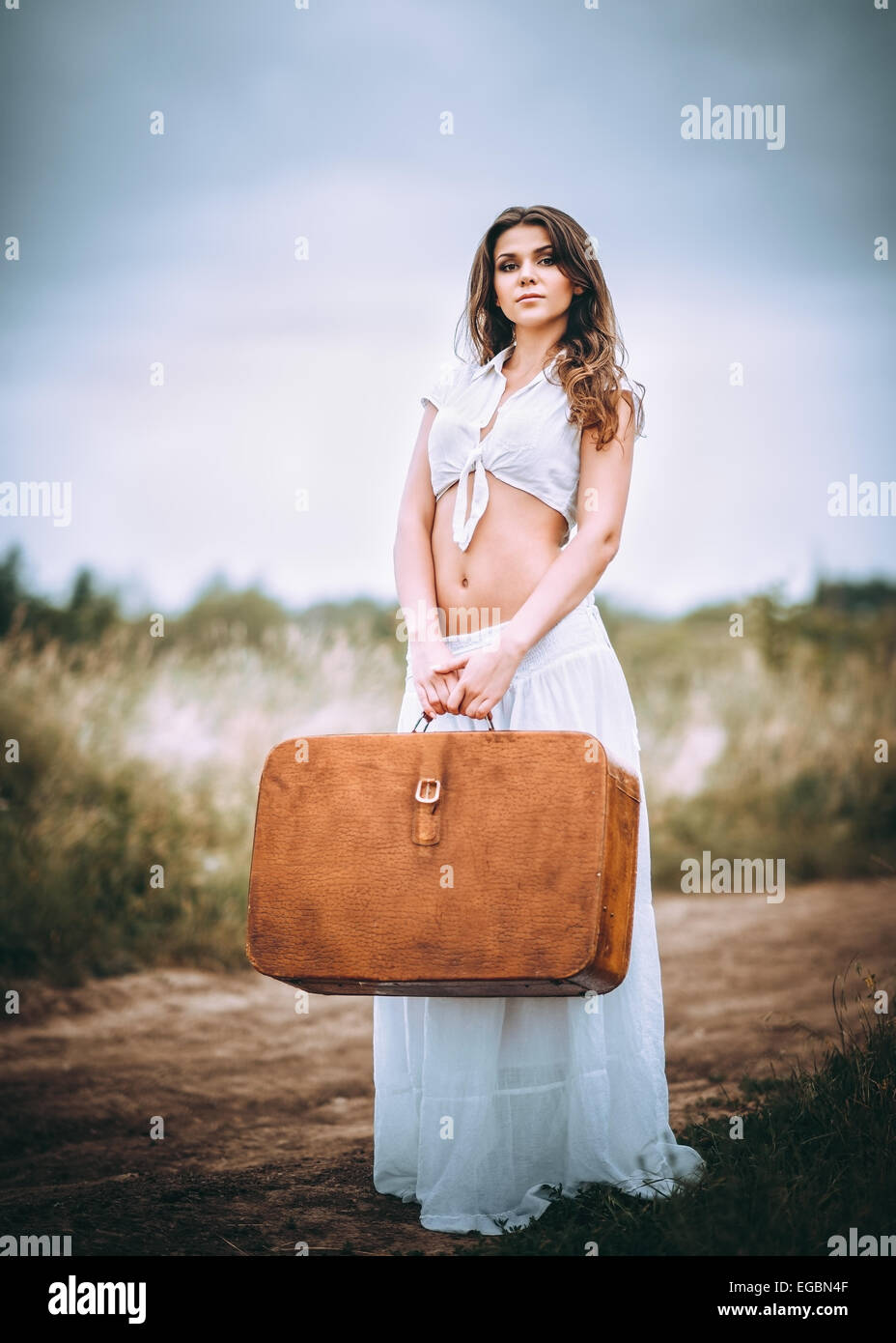 Belle jeune femme avec une valise à la main se dresse sur un field road Banque D'Images