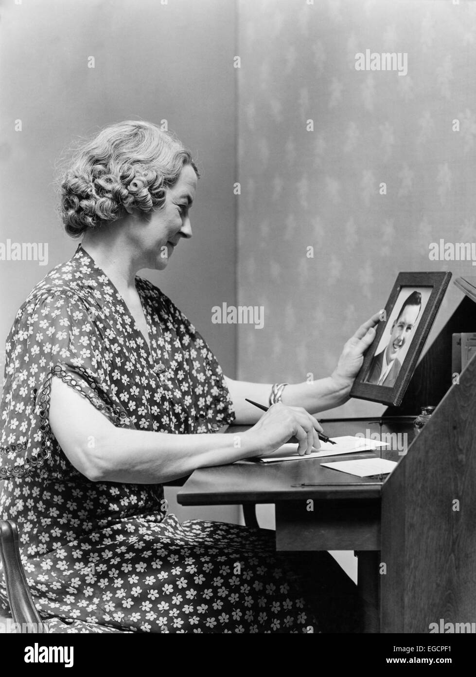 Années 1930 Années 1940 SENIOR WOMAN SITTING AT DESK ÉCRIT LETTRE COMME ELLE EST TITULAIRE D'PHOTO PORTRAIT DE JEUNE HOMME FILS Banque D'Images