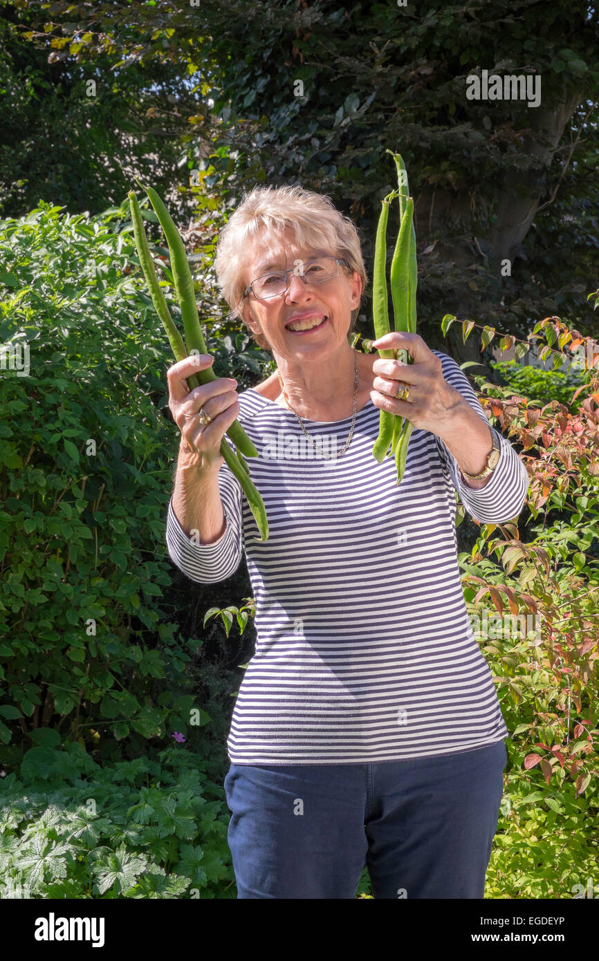 Femme plus âgée dans jardin avec grands haricots cultivés au jardin. Gloucestershire England UK Banque D'Images