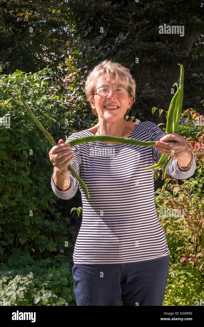 Femme plus âgée dans jardin avec grands haricots cultivés au jardin. Gloucestershire England UK Banque D'Images