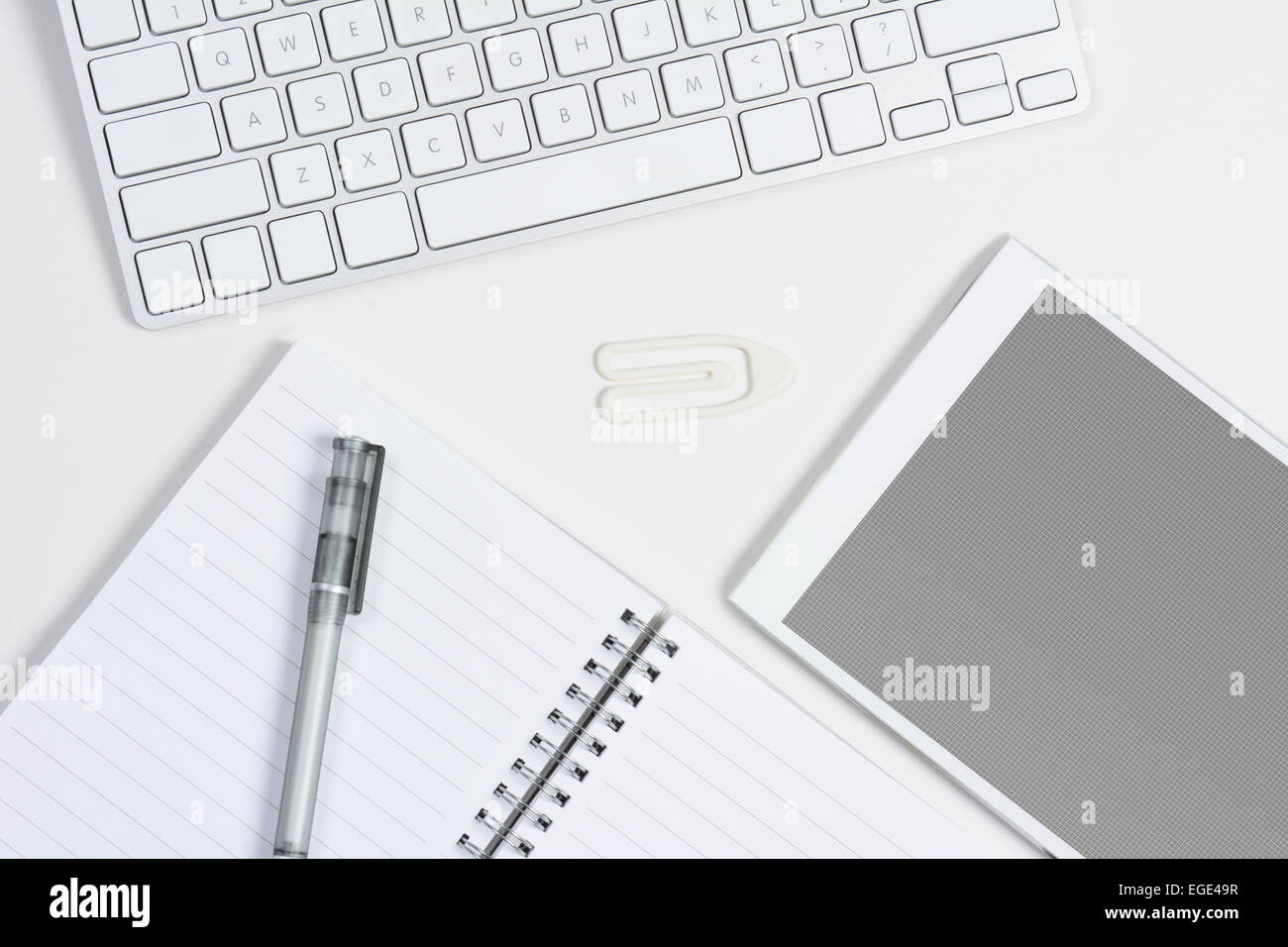 High angle shot d'un bureau à domicile bureau blanc avec clavier, tablette ordinateur avec un écran gris, grille et bloc-notes et un stylo. Banque D'Images