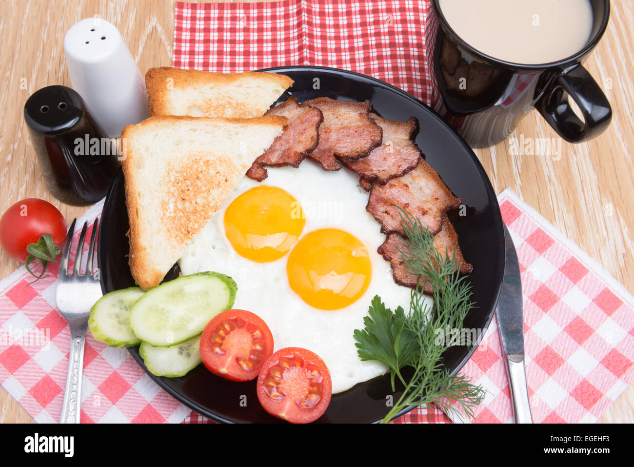 Oeufs au plat avec du bacon, du pain, du café et des légumes sur le plat noir Banque D'Images