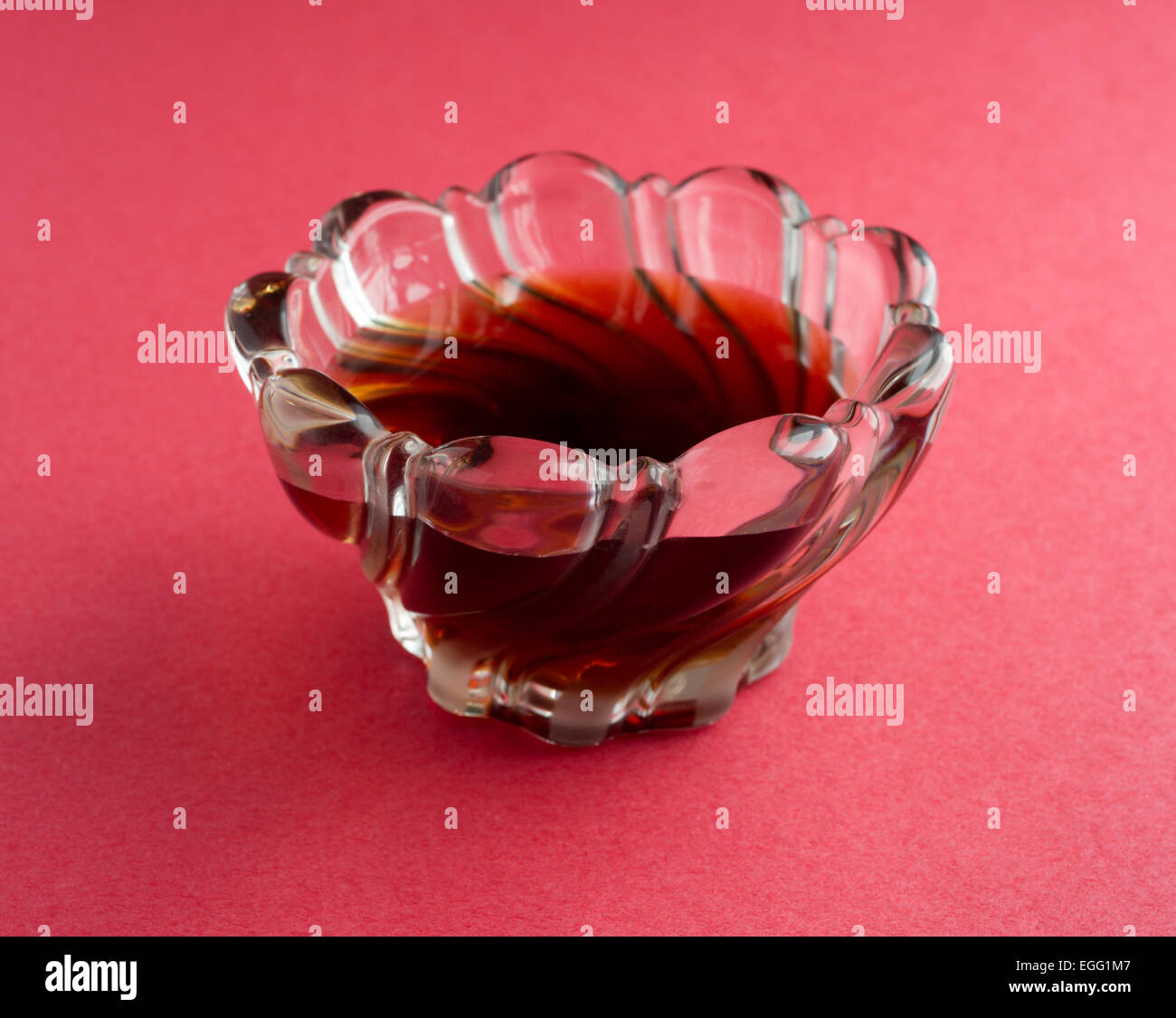 Vue latérale d'un bol en verre décoratif rempli de sirop d'érable sur fond rouge. Banque D'Images