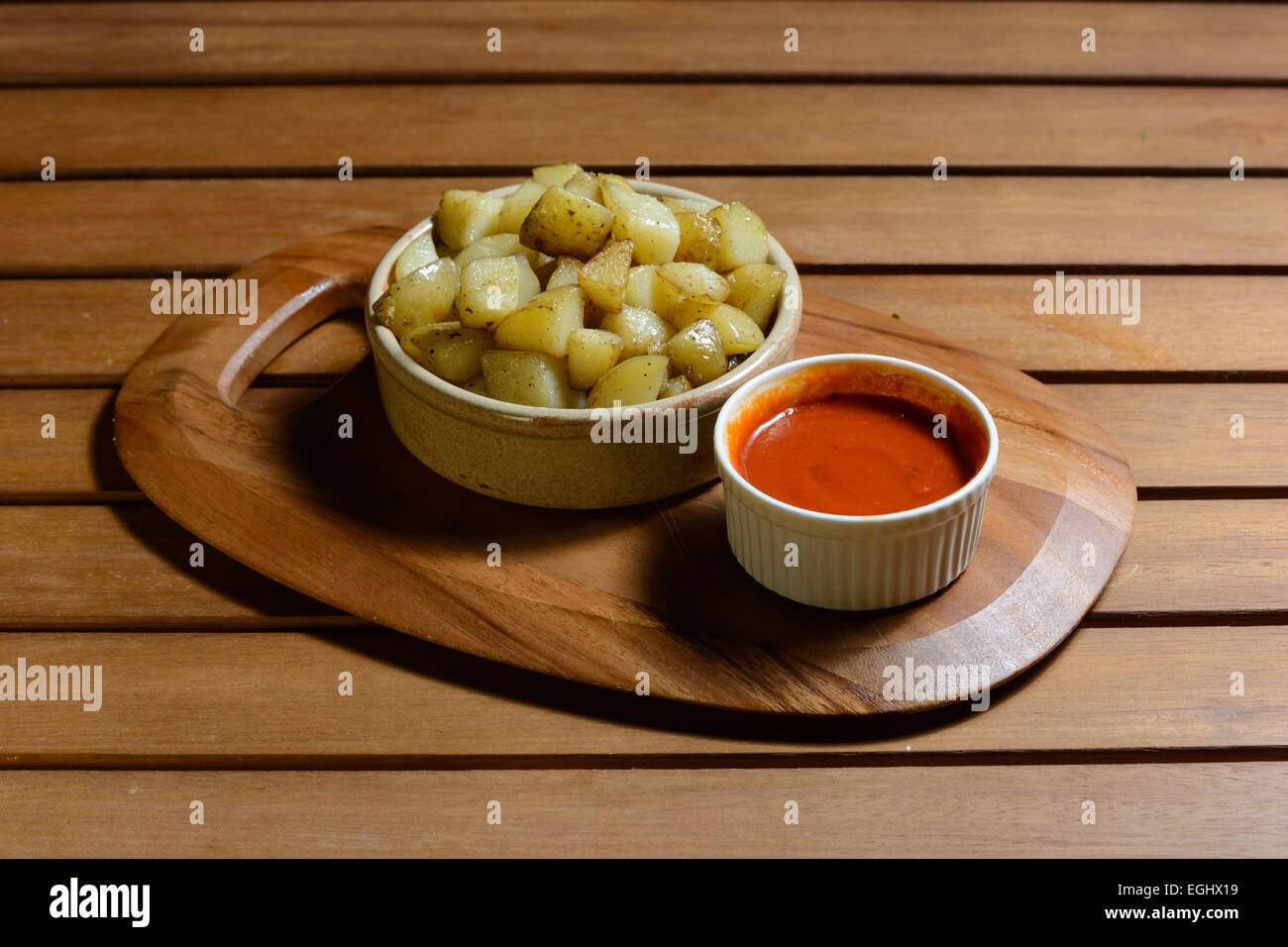 Tapas : patatas bravas. Dés de pommes de terre cuites avec de la sauce tomate épicée servi dans des bols en céramique sur une plaque de bois Banque D'Images