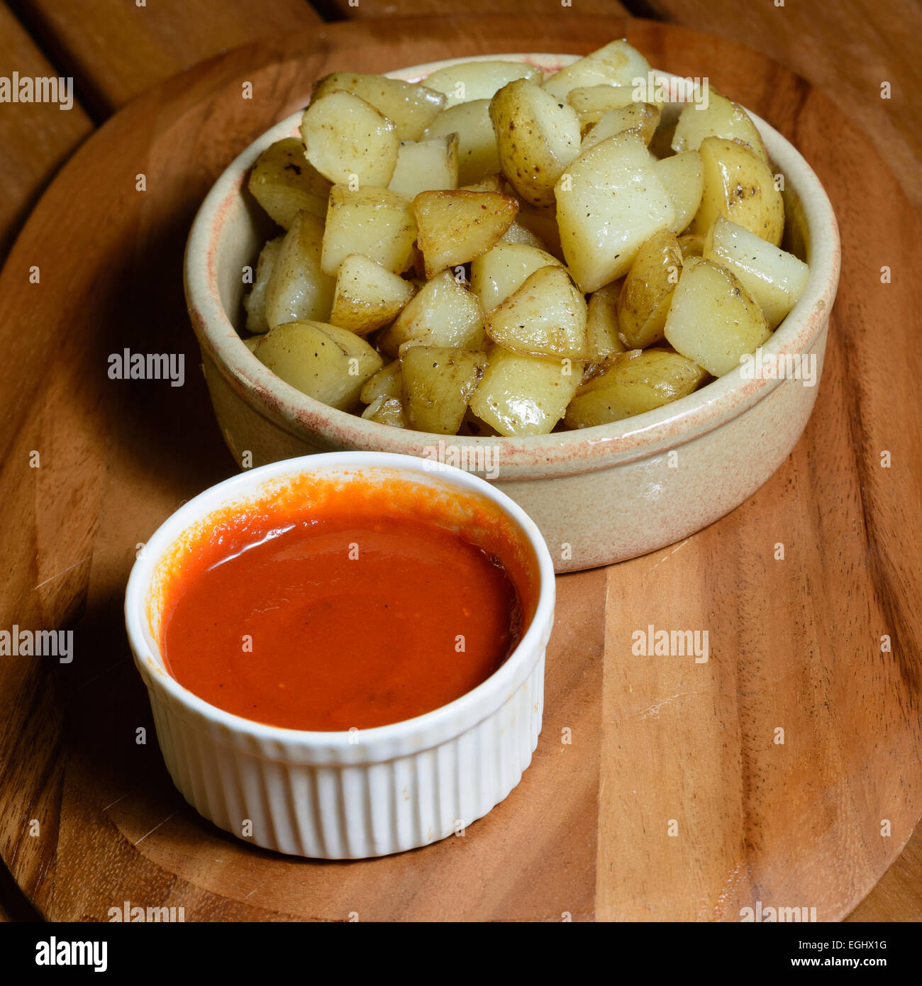 Tapas : patatas bravas. Dés de pommes de terre cuites avec de la sauce tomate épicée servi dans des bols en céramique sur une plaque de bois Banque D'Images