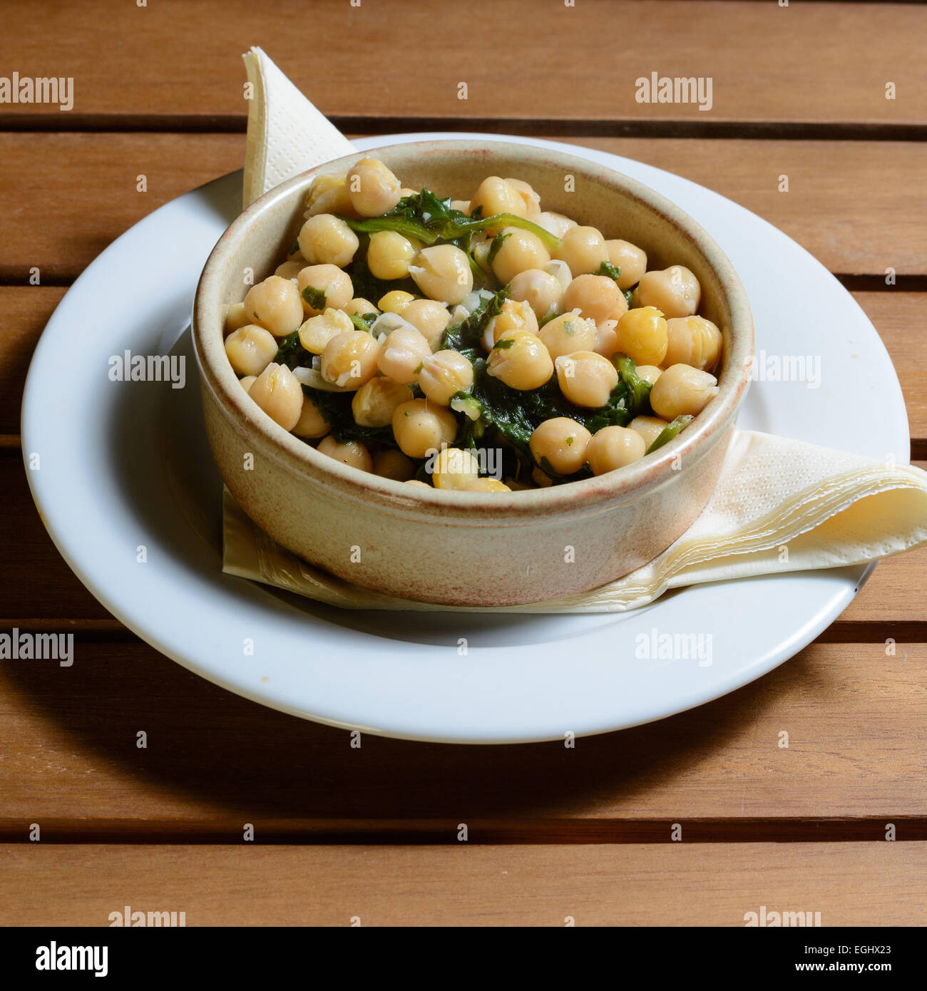 Des tapas. Les épinards et pois chiches cuits dans une sauce épicée, servi dans un bol en céramique marron sur une table en bois Banque D'Images