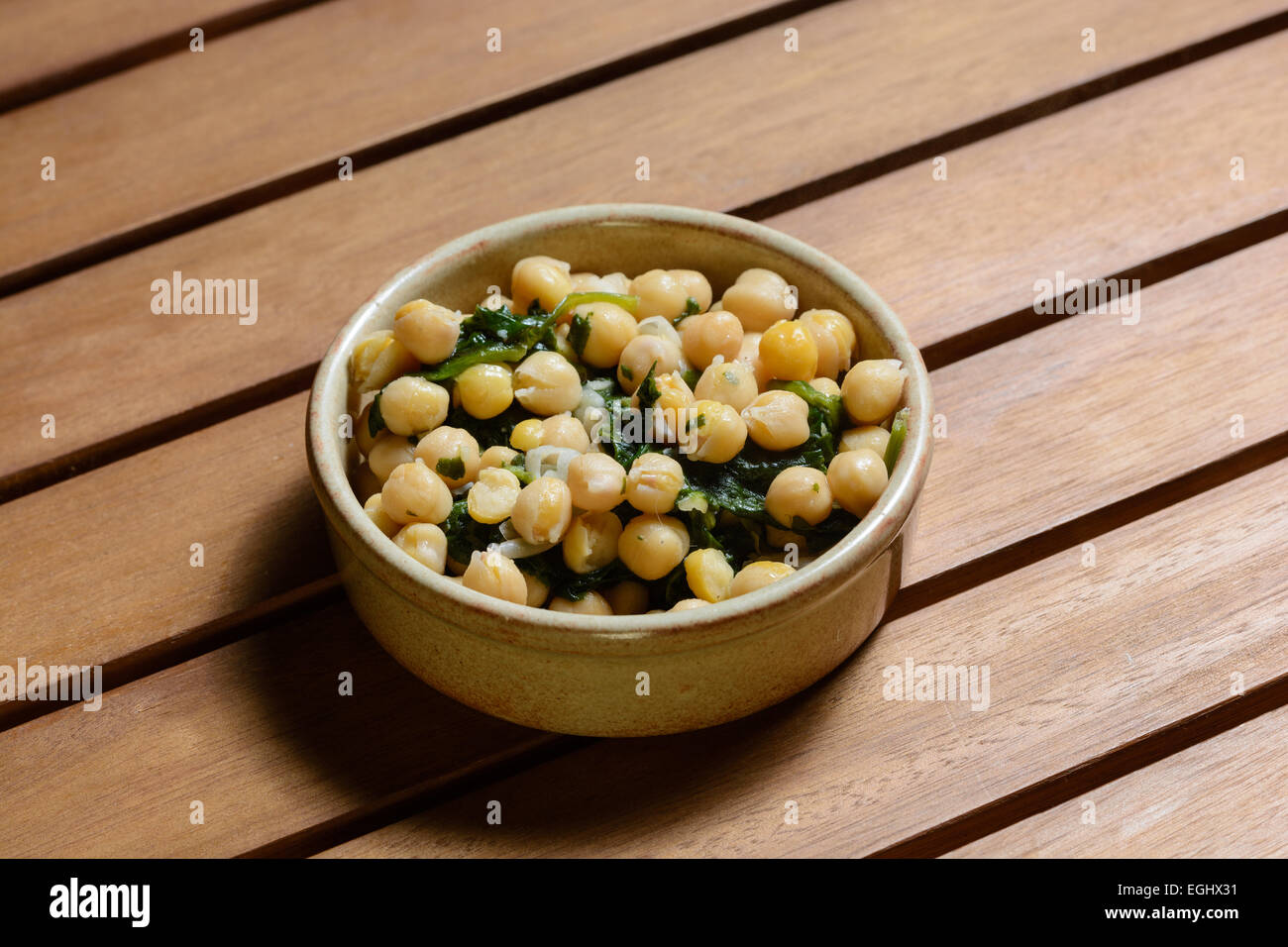 Des tapas. Les épinards et pois chiches cuits dans une sauce épicée, servi dans un bol en céramique marron sur une table en bois Banque D'Images