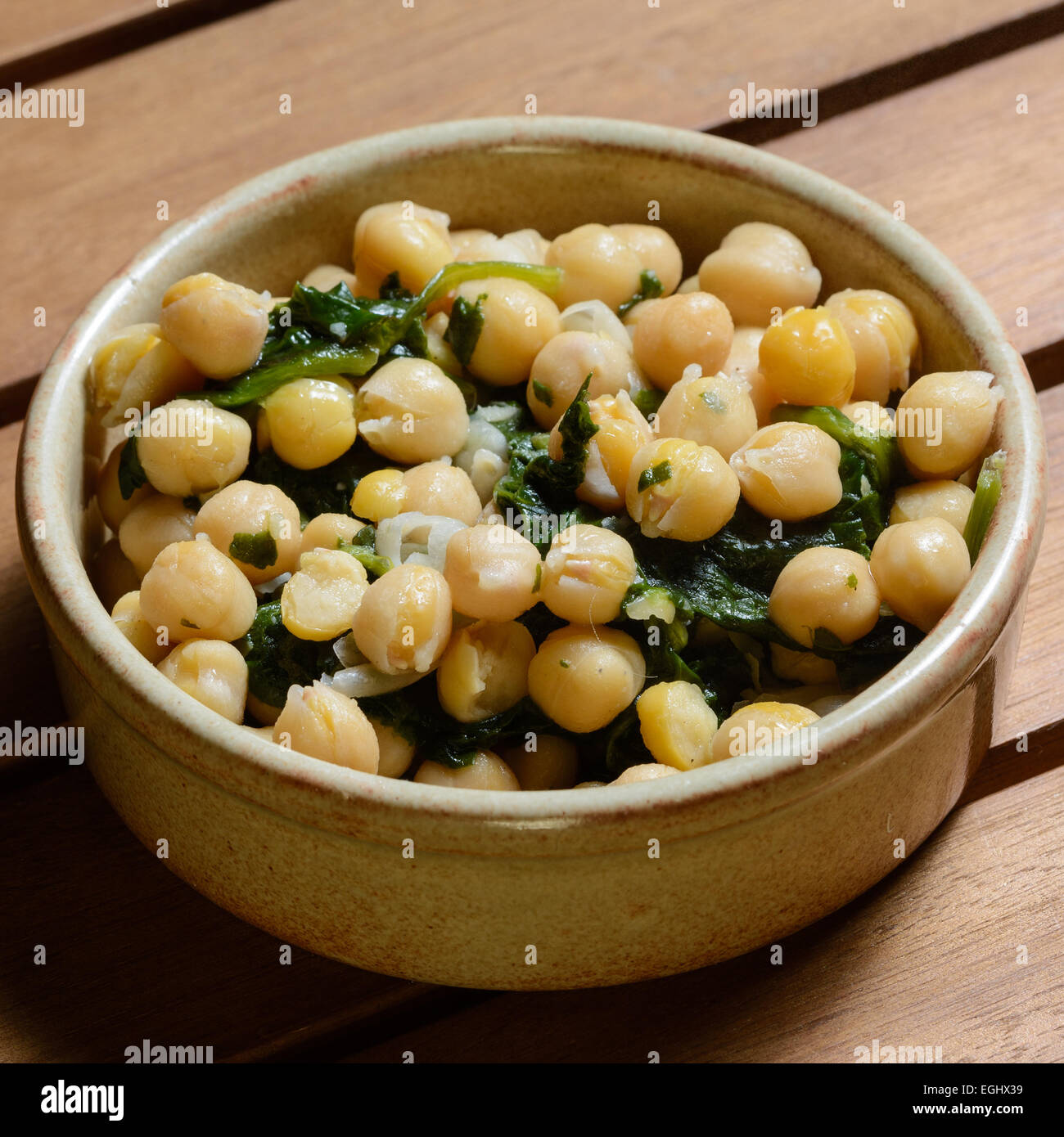 Des tapas. Les épinards et pois chiches cuits dans une sauce épicée, servi dans un bol en céramique marron sur une table en bois Banque D'Images