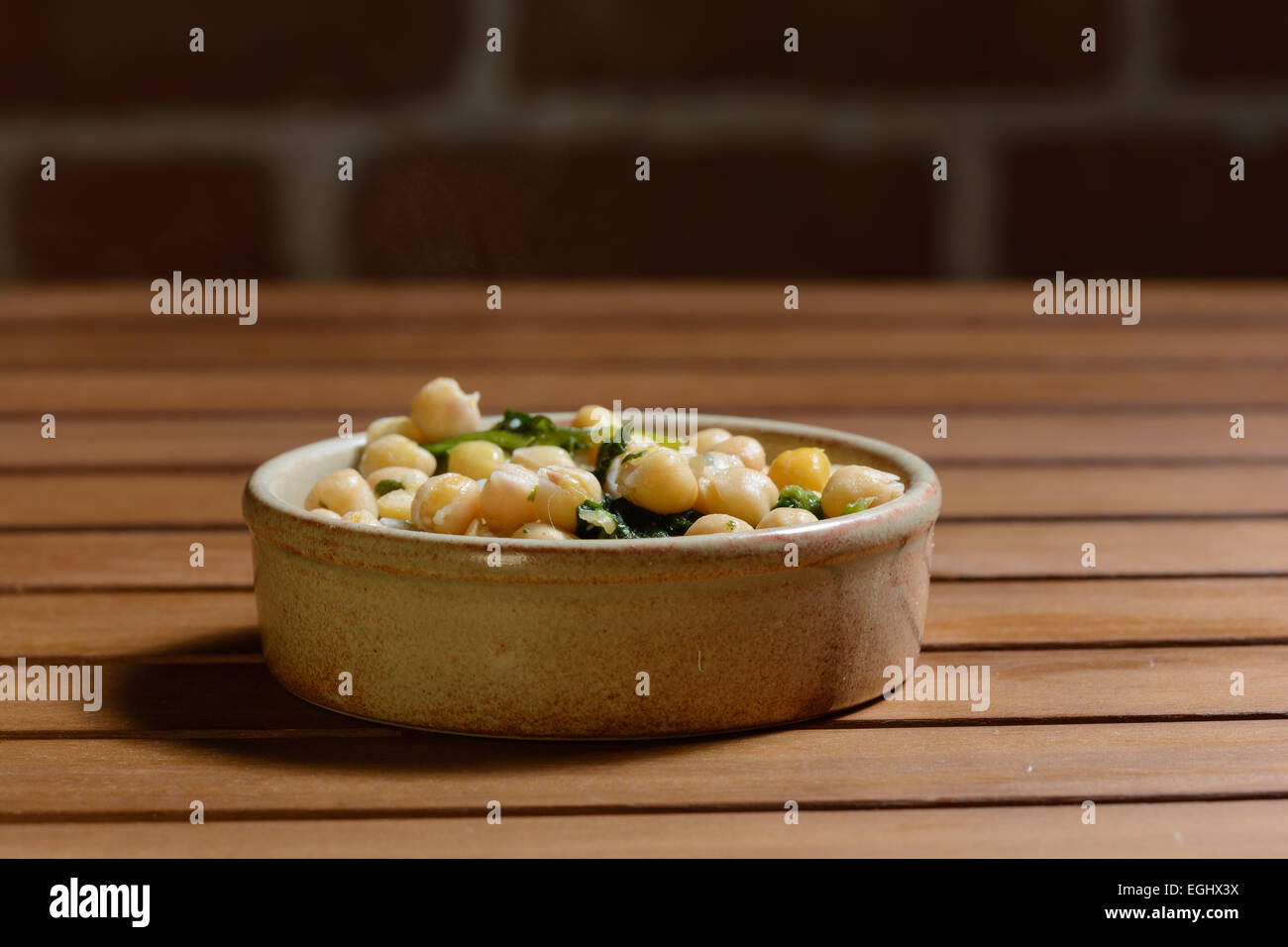 Des tapas. Les épinards et pois chiches cuits dans une sauce épicée, servi dans un bol en céramique marron sur une table en bois avec mur de brique Banque D'Images