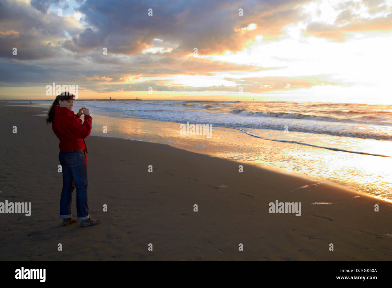 Femme de prendre une photo avec le soleil derrière le littoral de sable froid Banque D'Images
