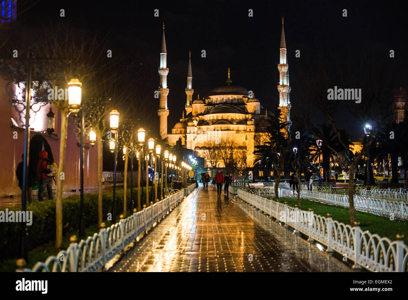 Mosquée du Sultan Ahmed vue nocturne Istanbul Turquie // ISTANBUL, Turquie — la Mosquée illuminée du Sultan Ahmed se reflète dans les pavés nichés par la pluie de la place Sultanahmet la nuit. Les dômes en cascade et les six minarets de la mosquée créent une silhouette spectaculaire sur le ciel du soir. La chaussée humide reflète les éléments architecturaux de la mosquée, doublant l'impact visuel de l'éclairage nocturne. Banque D'Images