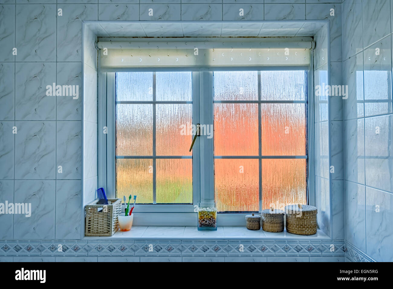 Salle de bains en verre dépoli avec distorsion de la fenêtre extérieure orange/bleu, et divers articles sur l'appui de la fenêtre. Banque D'Images