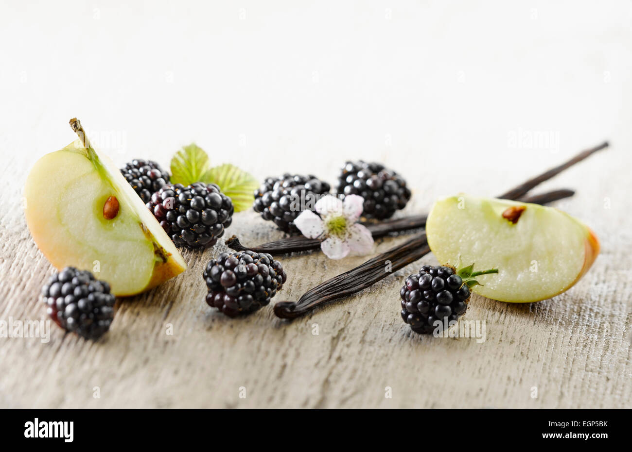 Blackberry, Rubus cultivar. Plusieurs baies organisées avec des fleurs et des feuilles et morceaux de pomme, plus pâle sur les gousses de vanille, en détresse, fond de bois. Focus sélectif. Banque D'Images