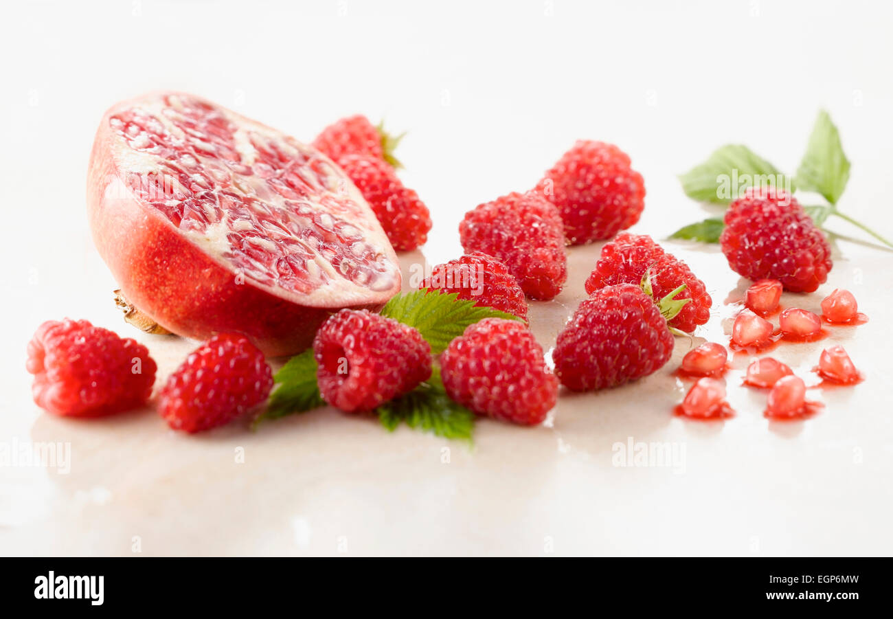 Framboisier, Rubus idaeus cultivar et Grenade, Punica cultivar réduit de moitié entouré de plusieurs framboises et feuilles sur le marbre blanc. Focus sélectif. Banque D'Images