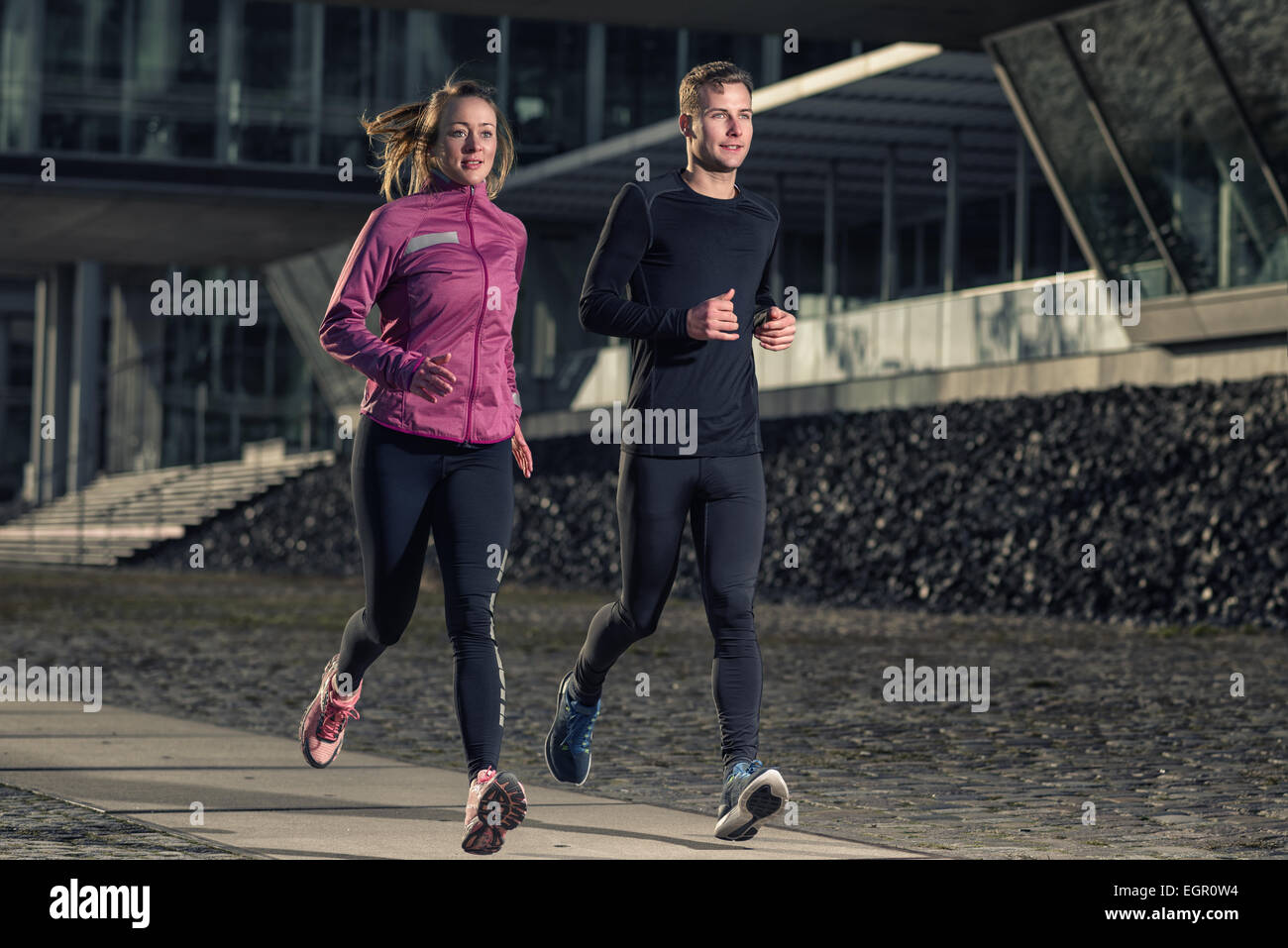 Jeune actif couple jogging côte à côte dans une rue urbaine au cours de leur entraînement quotidien dans un concept de santé et de remise en forme Banque D'Images
