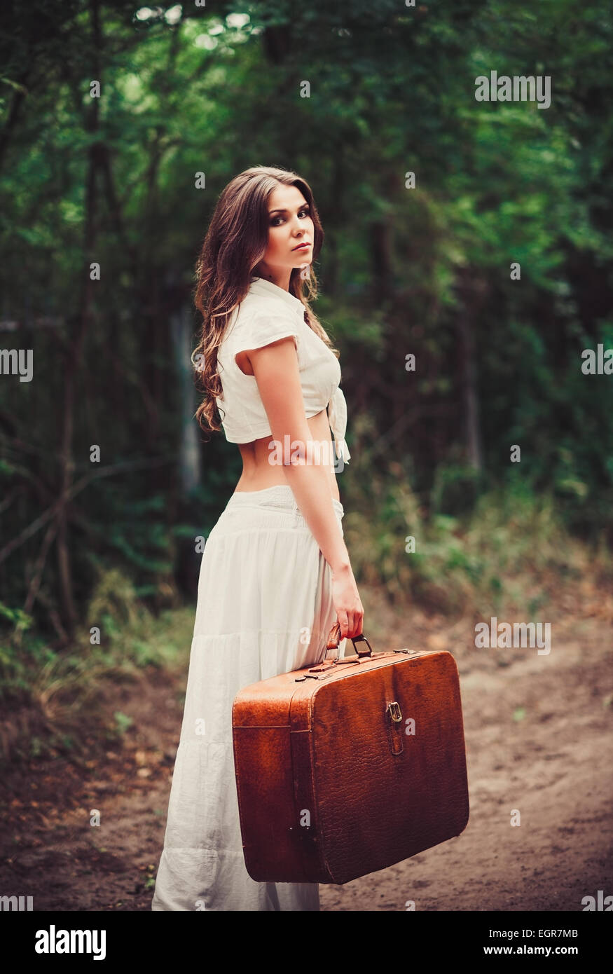 Belle jeune femme triste avec valise à la main debout sur une route Banque D'Images