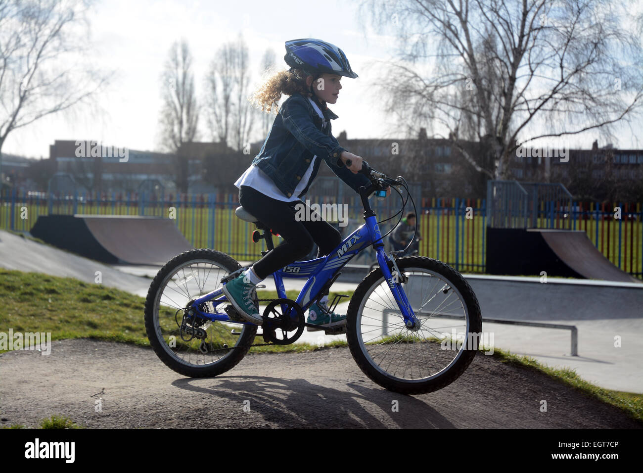 Sept ans, fille de porter un casque de vélo randonnée à vélo autour d'une piste de vélo BMX sur une froide journée d'hiver à Londres Banque D'Images