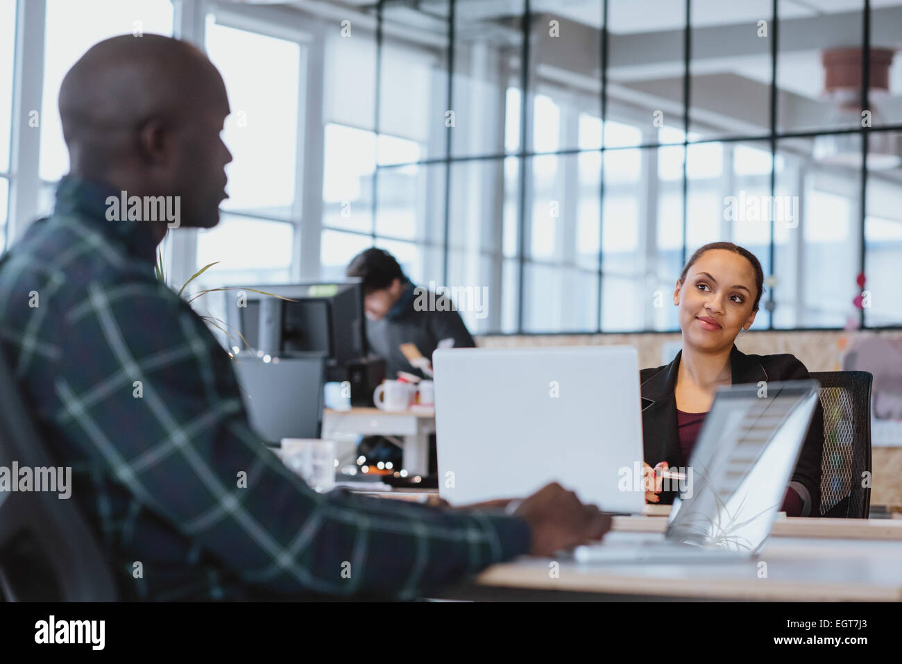 Jeune femme à la recherche de collègue masculin tout en étant assis à une table avec un ordinateur portable. African executive discuter travail avec un collègue. Banque D'Images