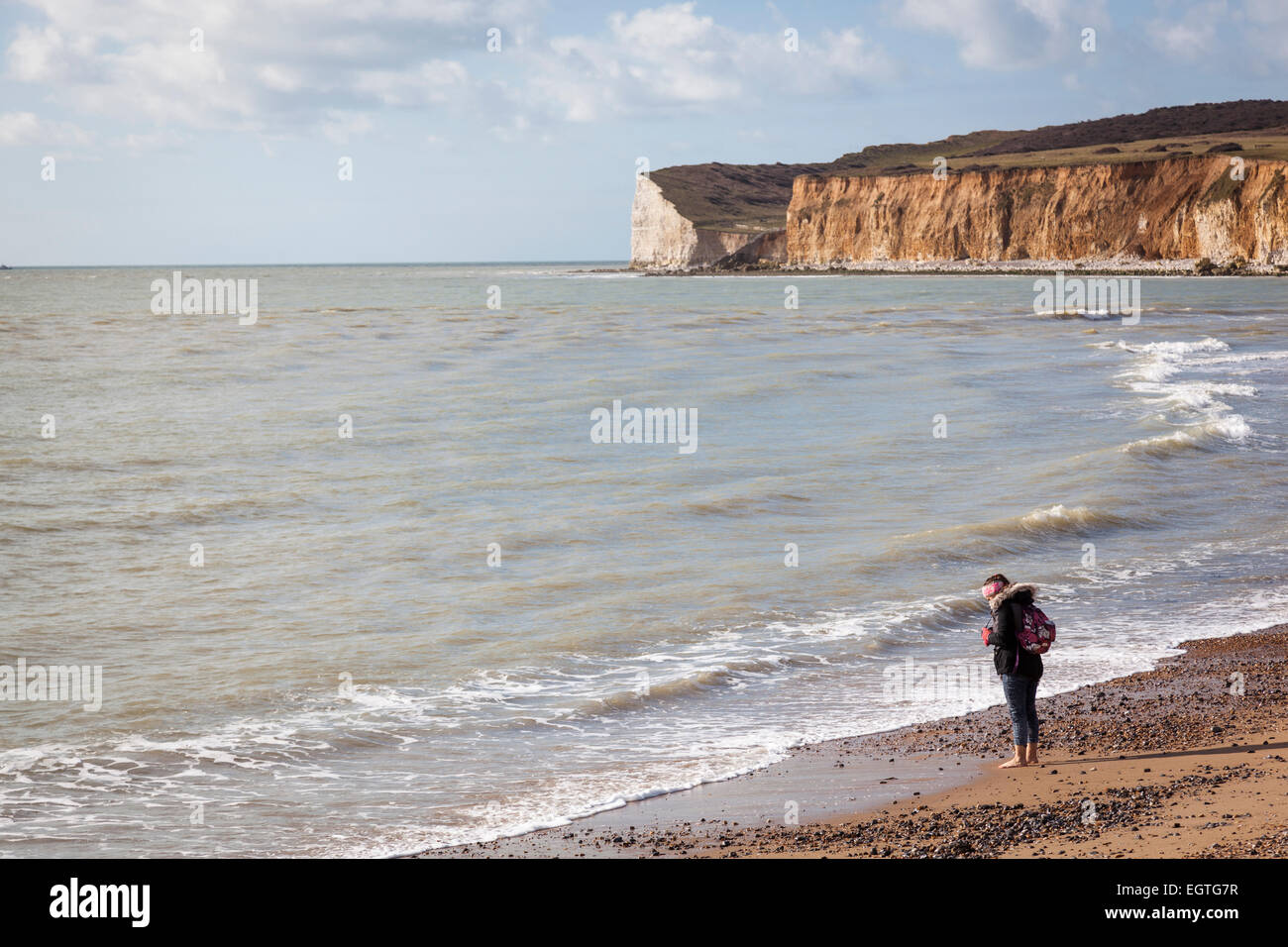 Une femme se prépare à barboter dans la mer, un jour d'hiver sur la plage de galets à Cuckmere Haven. Banque D'Images