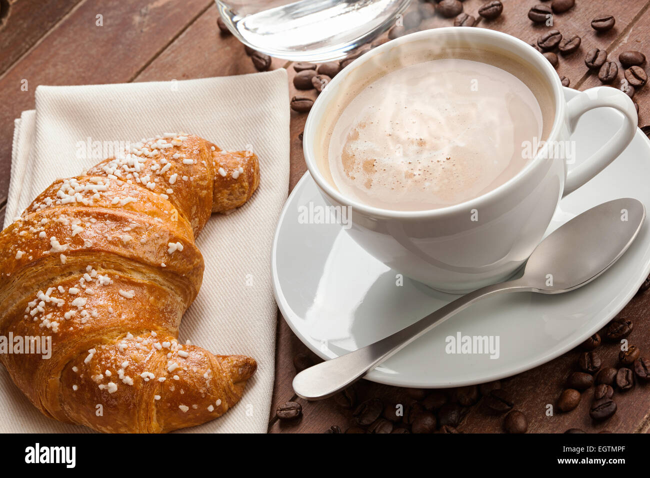 Cappuccino avec un croissant et un verre de l'eau dans le bac de bois marron foncé. Banque D'Images